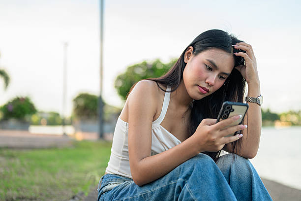 istock Young Asian Thai woman sitting and using phone outdoors while sitting in park 2236307321
