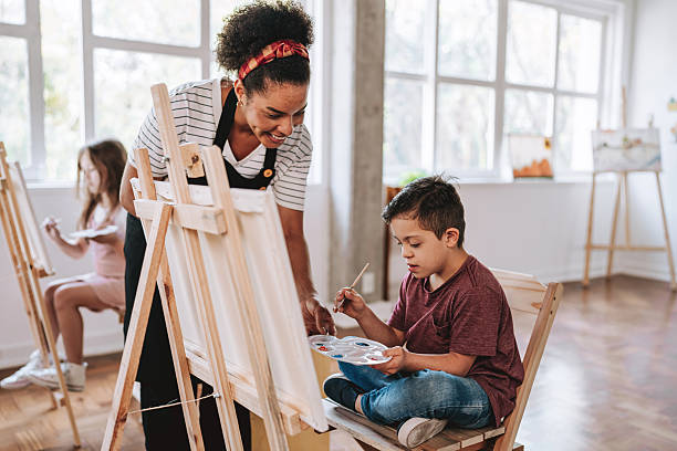 istock Teacher assisting a child with Down syndrome - painting class on canvas 2236313764