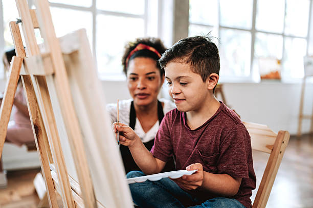 istock Teacher assisting a child with Down syndrome - painting class on canvas 2236313771