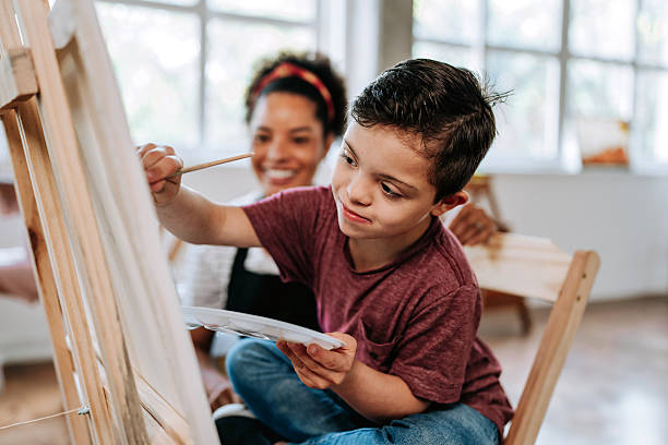 Teacher assisting a child with Down syndrome - painting class on canvas