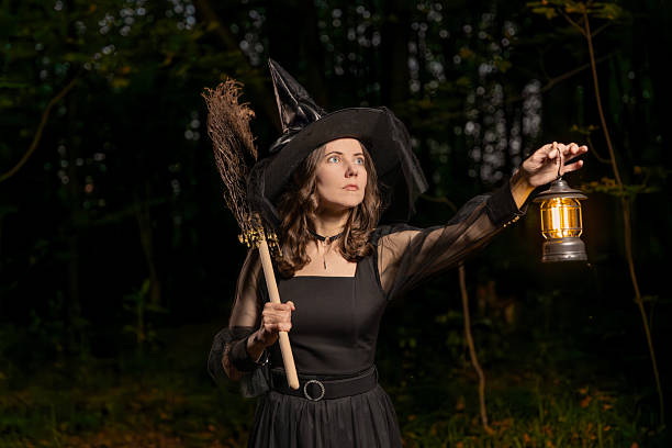 istock Halloween witch with broom holding glowing lantern in dark forest at night 2236316460