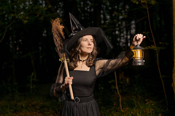 istock Halloween witch with broom and glowing lantern in dark forest at night 2236317223