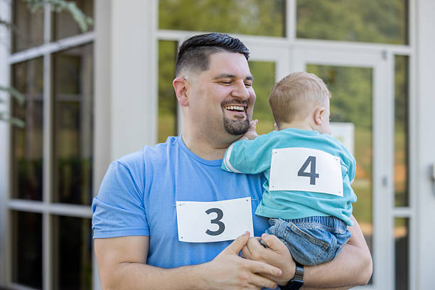 Happy father holds his toddler son who has Down Syndrome while attending community marathon to benefit charity