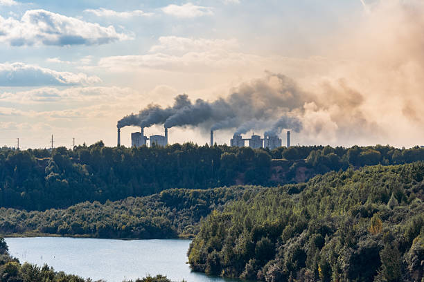 Industrial factory chimneys emit thick smoke over a green forest and river, highlighting environmental pollution and its impact on nature and air quality. stock photo