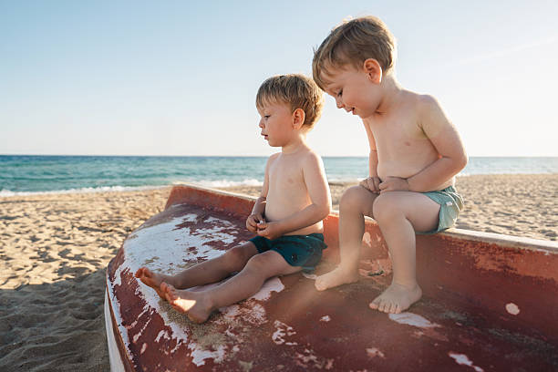Twin brothers are enjoying a relaxing day at the beach, sitting on an old boat and playing