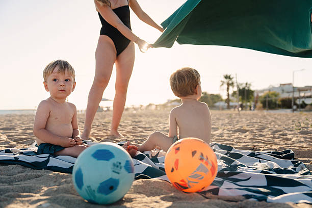 Mother prepares a beach towel for her children on a sandy beach during summer vacation