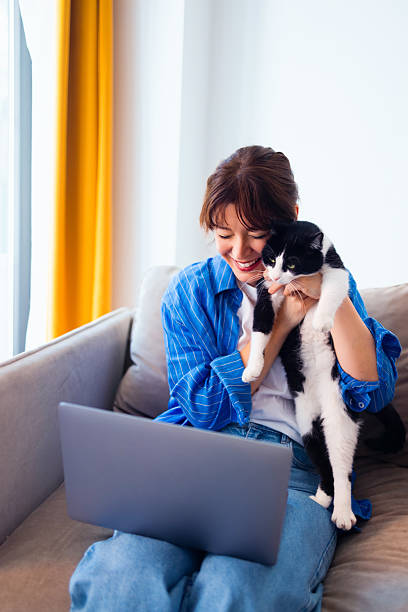 istock Woman Sitting on a Couch Holding a Cat While Using a Laptop 2236326559