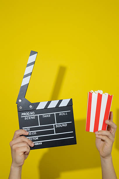 istock Hands holding a movie clapperboard and popcorn on a yellow background with copy space 2236328488