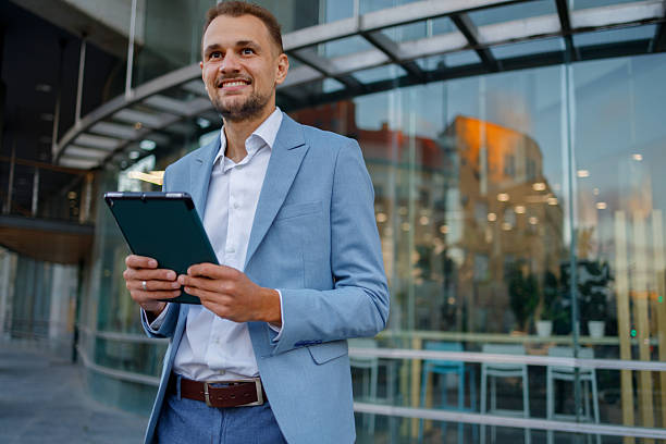 istock Professional businessman using digital tablet outdoors, standing confidently in front of a modern corporate building 2236332481