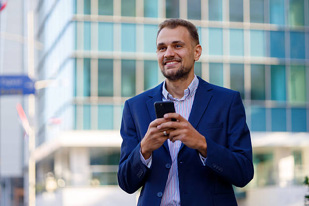 istock Happy businessman using smartphone in urban setting, smiling and looking away, standing against modern building 2236332574