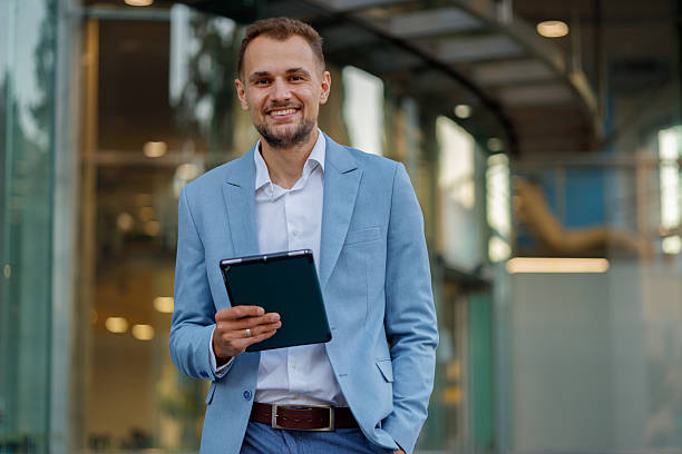 istock Smiling businessman using digital tablet, standing confidently outside a modern office building 2236332578