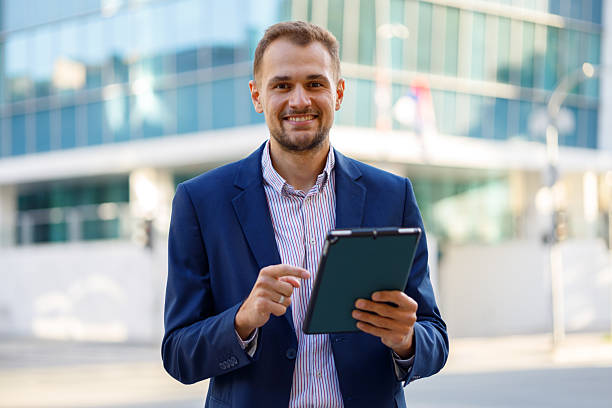 istock Confident businessman using a tablet for work, standing in an urban environment with a blurred office building background 2236333200