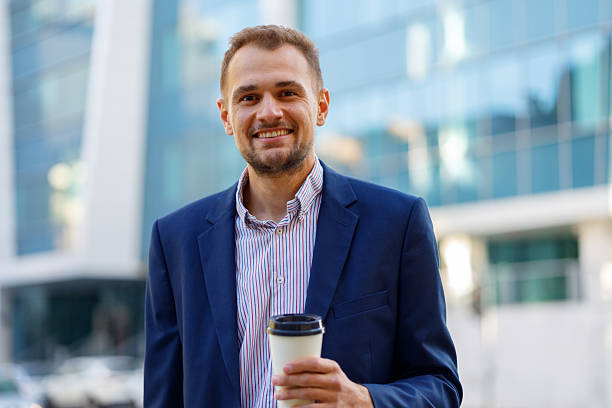 istock Smiling businessman holding coffee cup standing outdoors, looking at camera in urban setting 2236333257