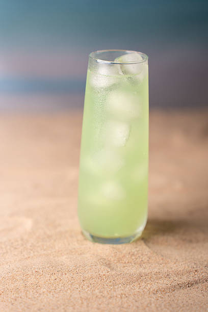 istock refreshingly cool green beverage in a tall glass with ice cubes placed on sandy beach with soft focus ocean and sky background creating a tranquil and relaxing summer atmosphere, tropical, elegant 2236333329