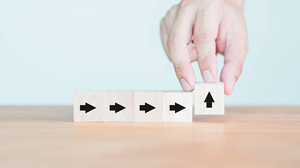 istock Hand arranging wooden cube blocks with arrows and one upward arrow, symbolizing change, growth, and innovation, placed on a wooden table against a light background. 2236342835