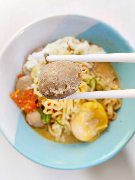 A tempting bowl of hot instant noodle soup with savory meatballs, a soft-boiled egg, and a spicy kick, perfect for a quick, comforting meal.