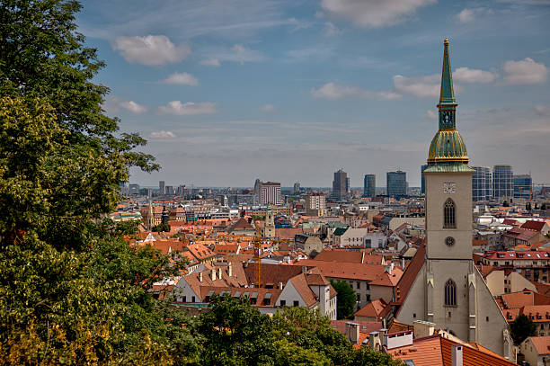 Bratislava, Slovakia – July 24, 2025: Rooftop view over Bratislava’s Old Town reveals a patchwork of tiled gables, dormer windows, and colorful facades, blending Baroque and modern elements across a layered skyline of residential and religious architecture.