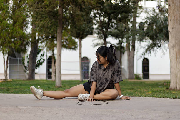 Young woman in casual workout clothes sits on the ground in a park stretching her leg, focusing on flexibility and self-care while enjoying an active, healthy outdoor moment