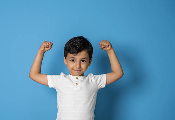 Cute little boy showing his biceps on blue background