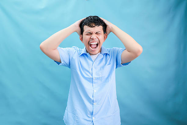 A man expressing frustration, gripping his head against a light blue backdrop.