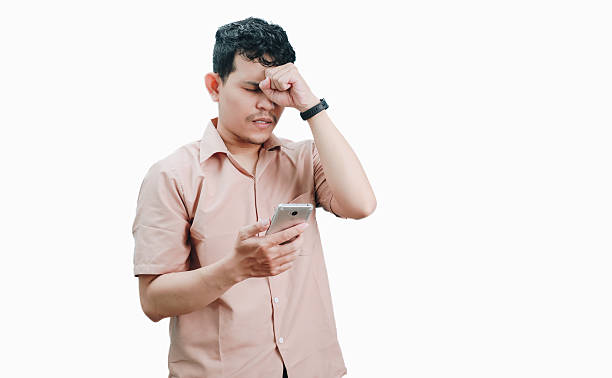 istock Young man rubbing his eye while looking at his smartphone, experiencing eye strain or discomfort from screen use. 2236361315