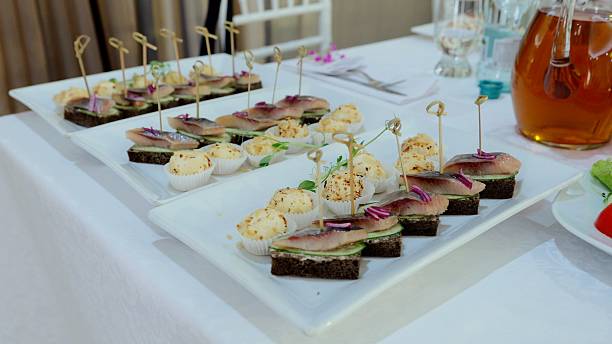 istock Pickled herring sandwiches layered with cucumber and red onion slices resting on white rectangular plates, prepared for catered event serving 2236363241