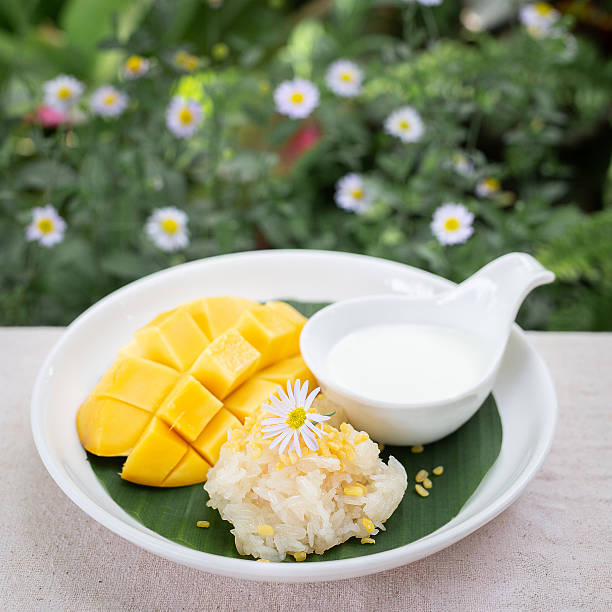 Mango Sticky Rice Dessert, Traditional Thai dessert with ripe mango slices, sweet sticky rice topped with mung beans, and coconut milk served on banana leaf.