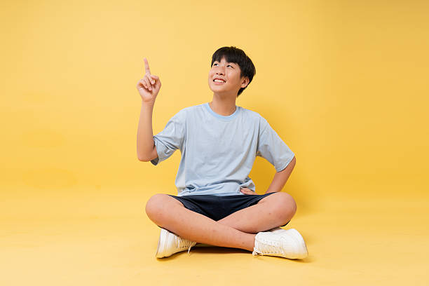 istock Boy Sitting Cross-Legged with Finger Pointing Up: A positive and bright optimistic expression 2236369368