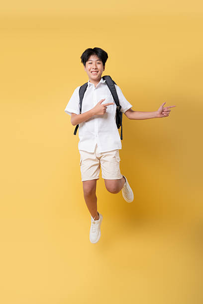 istock Energetic student jumps for joy ready for school with backpack and pointing on yellow background 2236372177