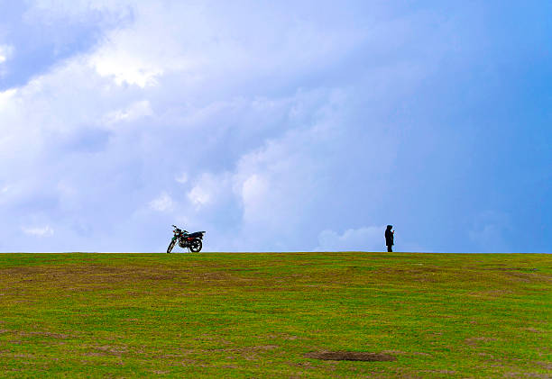 Silhouette of man and motorcycle on grassy hill under dramatic cloudy sky.