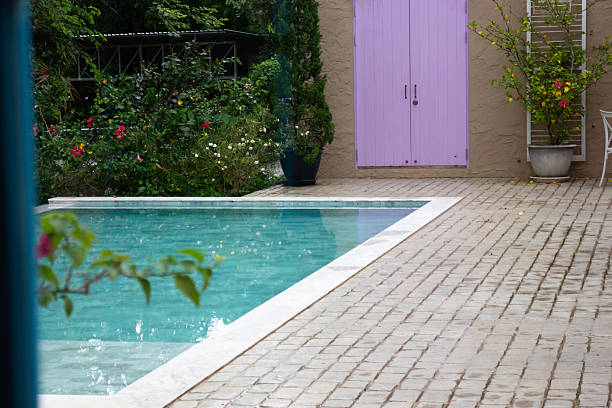 A serene backyard with a swimming pool, lounge chairs, a swing, and decorative plants. The clean white stone path and lush greenery create a relaxing atmosphere for outdoor leisure.
