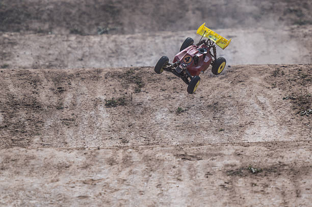 Red and yellow radio-controlled car flying over a jump on a dirt track, creating a dynamic and exciting scene