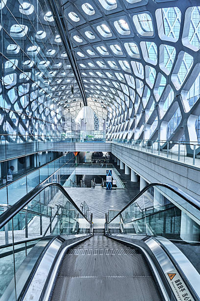 Munich, Germany - June 21, 2025: Spacious departure lounge at Munich International Airport in Germany, photographed in a panoramic style. Rows of grey seats line the bright concourse as travellers sit, read and use their phones while waiting to board. Floor to ceiling windows stretch across the scene, revealing other terminal buildings, aircraft stands and activity on the apron outside.