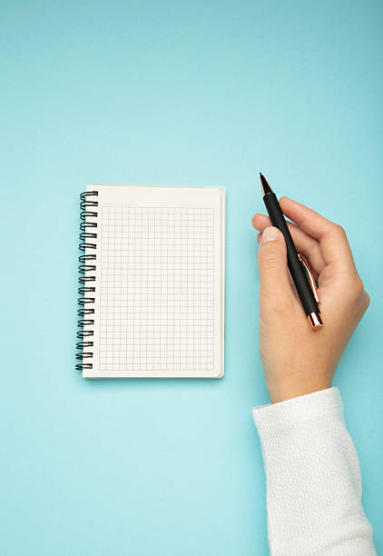 istock Female's hand writing in white blank open spiral notebook with pen on pastel blue background. Flat lay, copy space. 2236385043