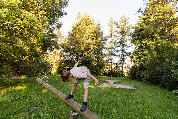 istock Two children play happily in a park surrounded by trees. One child balances on a log while the other plays nearby, enjoying a sunny afternoon in nature 2236387165