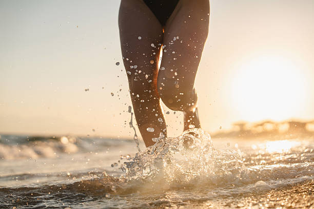 istock Woman splashing waves while running on the beach at sunset 2236415944