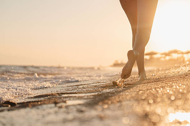Woman walking by the sea at sunset ,unrecognizable person, low section