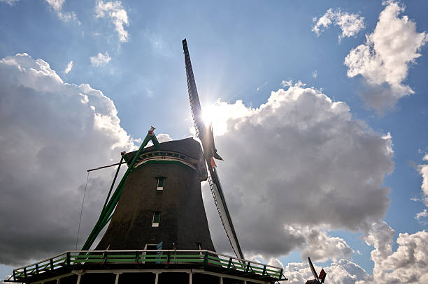 Traditional dutch windmill silhouetted against a cloudy blue sky with sunlight