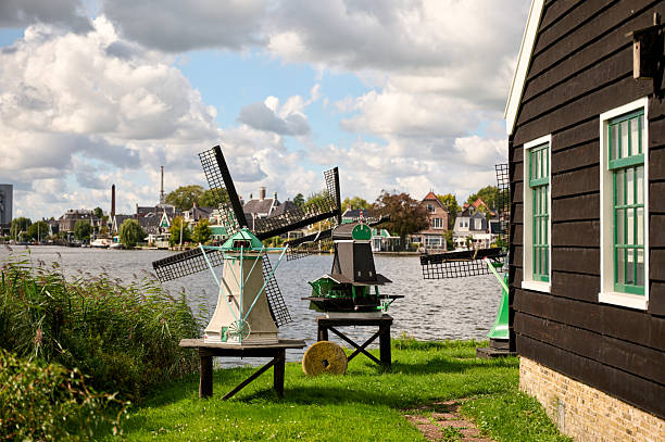 Miniature windmills standing on green grass next to a canal with traditional dutch houses in the background