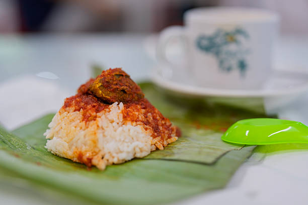 Close-up of nasi lemak with sambal and rice wrapped in banana leaf, traditional Malaysian breakfast served with coffee in the background.