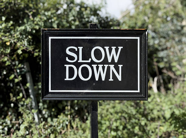 Slow Down sign white text on black - blurred vegetation background