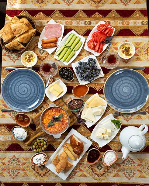 A colorful traditional breakfast spread showcases an array of foods including breads, vegetables, fruits, cheeses, and dips, arranged elegantly on a beautifully patterned tablecloth.
