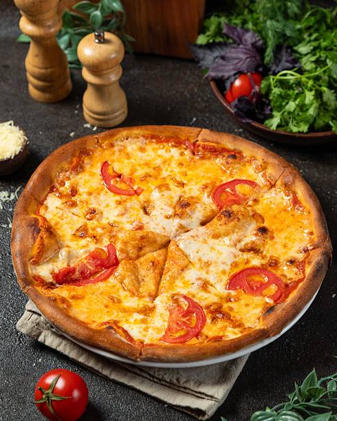 istock Freshly baked pizza with tomatoes and cheese served on a rustic table surrounded by greens and seasonings 2236437027