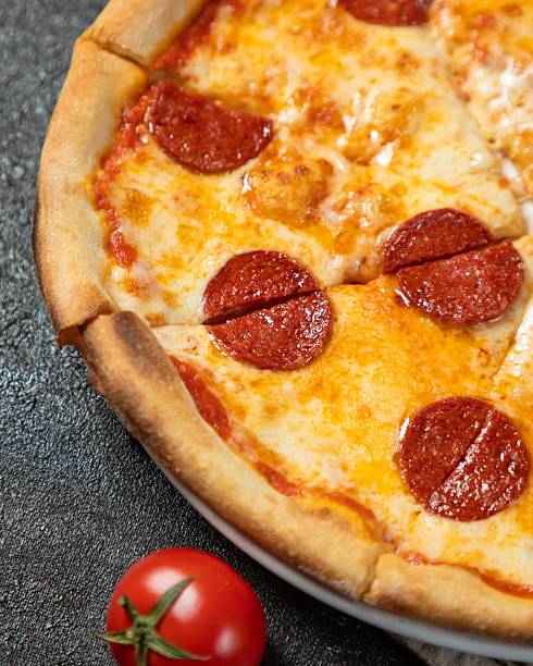 istock Delicious pepperoni pizza served fresh with a vibrant red tomato on a dark stone surface 2236437086