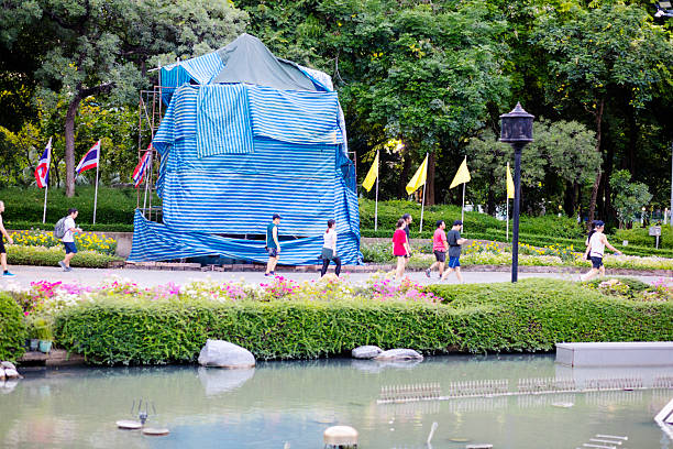 Running and exercising thai people in Benchasiri Park at early evening and sunset time. People are  passing between a pond and trees in background. People have different ages. Some pennants are haning at line. Park is located at Sukhuvit Road in Bangkok Khlong Toie. View from sidewalk of Sukhumvit Road.