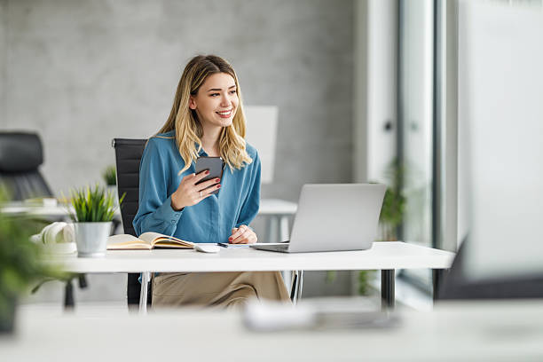istock Young woman engaged in work at a modern office using a laptop and smartphone during daytime hours 2236452369