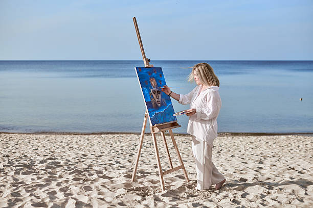 istock Young female artist painting on tranquil beach setting 2236455705