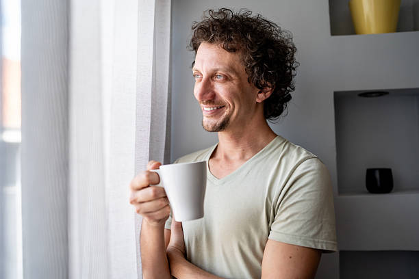 istock Smiling Man With Coffee Mug Standing By Window in Morning Light 2236467675