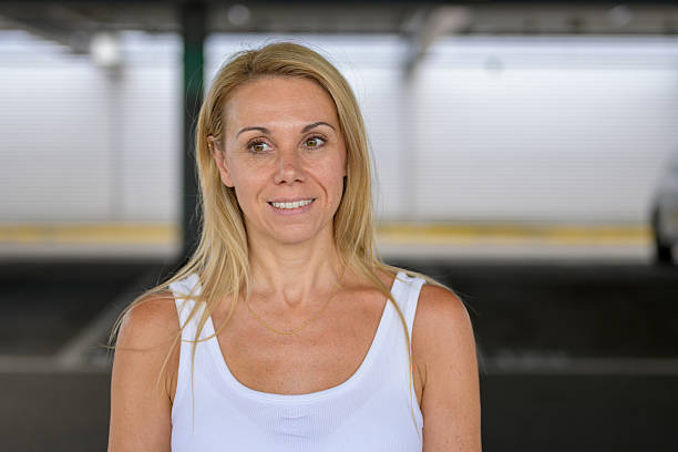 Portrait of a blonde woman in a white tank top, smiling gently while looking slightly to her left.