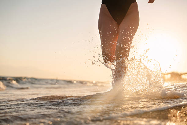 istock Woman splashing waves while running on the beach at sunset 2236471975